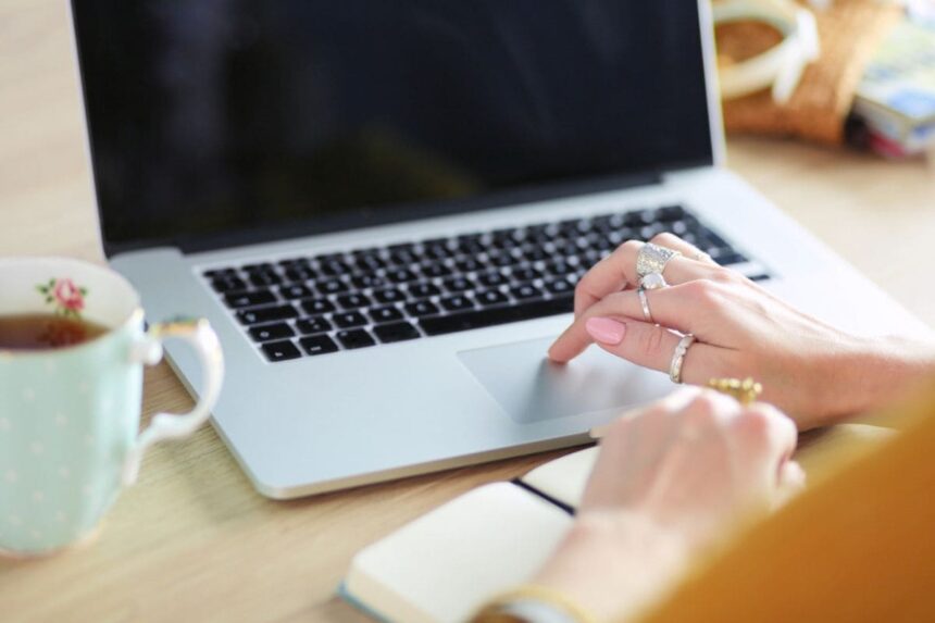 A freelance writer working from a home office desk, using a laptop and drinking coffee.