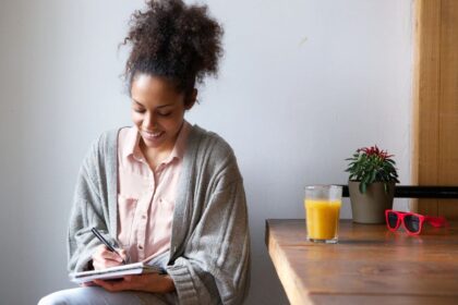 A woman sitting at home at a kitchen table, writing in a notebook.