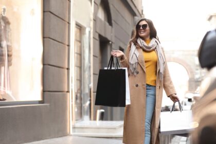 A mystery shopper, walking outside a store front, holding shopping bags.