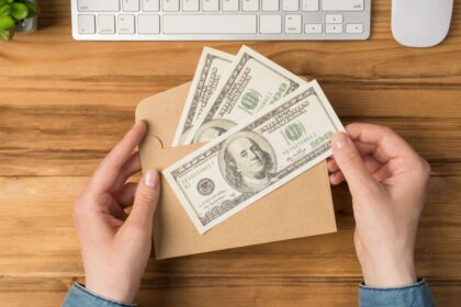 A woman sitting at a home office desk, counting cash in an envelope from a second income job.