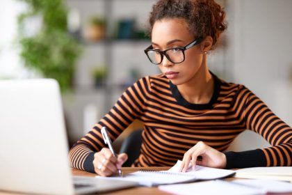 A woman working from home on a business plan, and writing in a notebook.